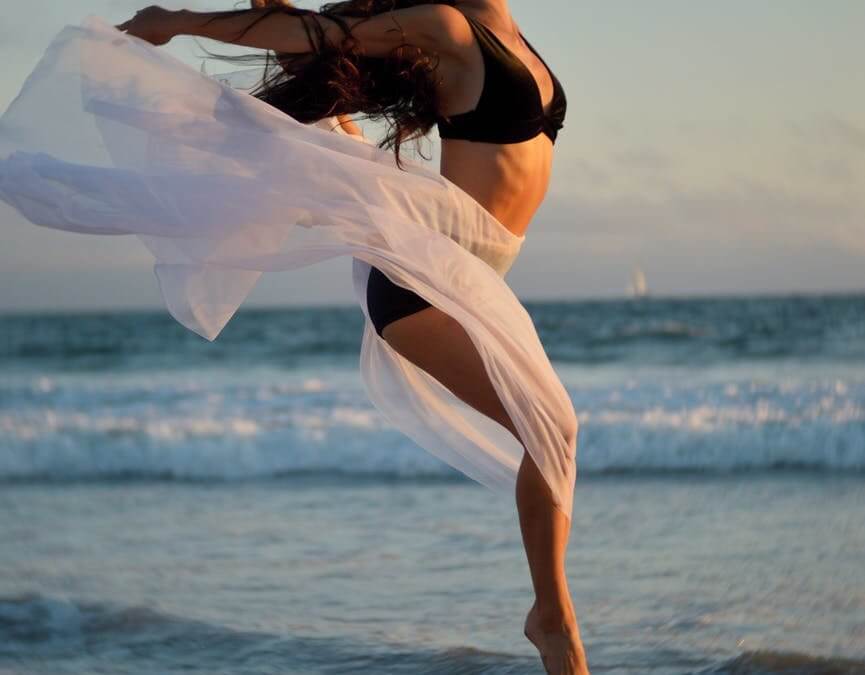 skinny dancer jumping over sandy shore of ocean